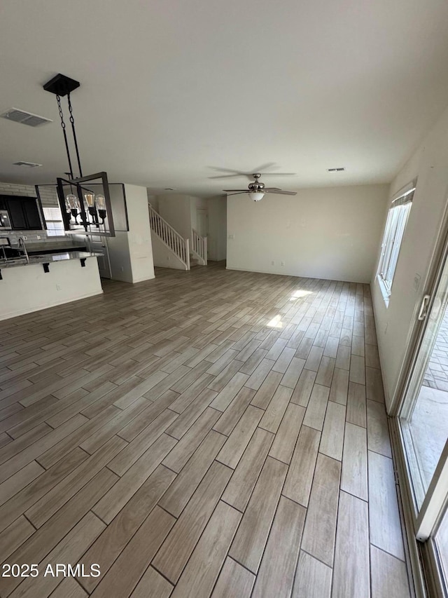 unfurnished living room with visible vents, stairs, ceiling fan, and wood tiled floor