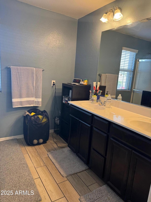 full bathroom with a sink, an enclosed shower, wood finish floors, and double vanity