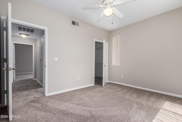 unfurnished bedroom with a walk in closet, carpet floors, a closet, and ceiling fan