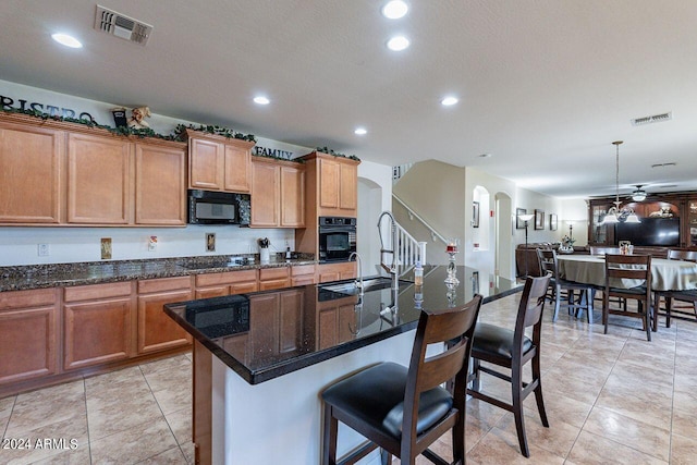 kitchen with a kitchen island with sink, dark stone counters, a kitchen bar, light tile patterned floors, and black appliances