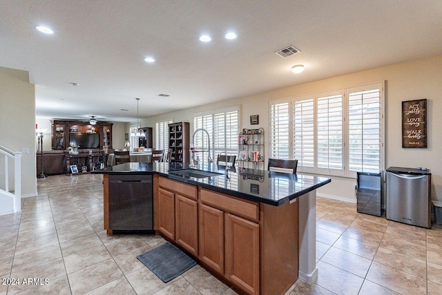 kitchen with dark stone countertops, sink, black dishwasher, an island with sink, and pendant lighting