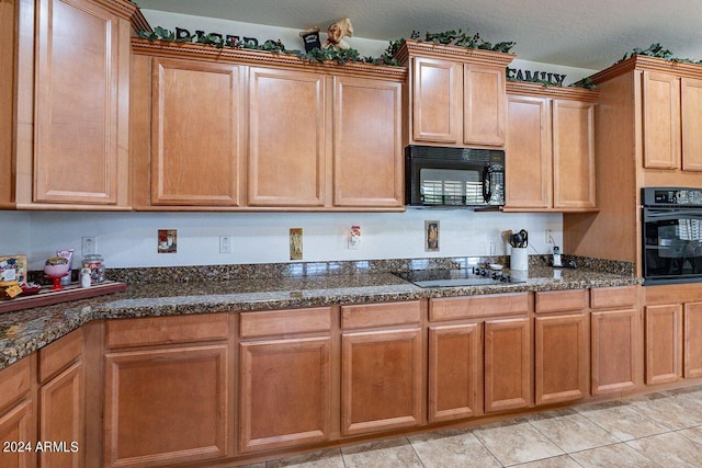 kitchen featuring a textured ceiling, black appliances, light tile patterned floors, and dark stone counters