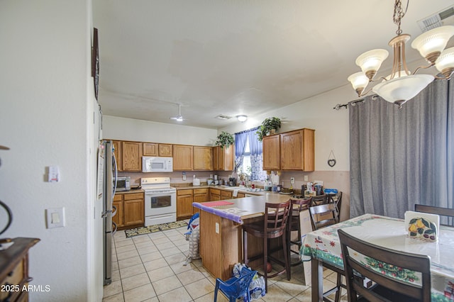 703 N Redwood Ln, Buckeye, AZ 85326 - kitchen with white appliances, light tile patterned flooring, brown cabinets, and a peninsula