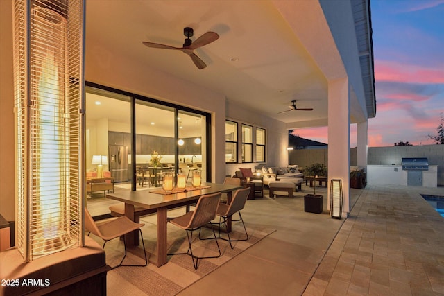 patio terrace at dusk with an outdoor living space, an outdoor kitchen, a grill, and ceiling fan