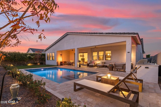 pool at dusk with an outdoor living space with a fire pit, a patio, ceiling fan, and exterior kitchen