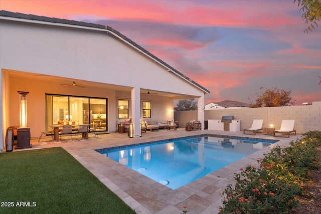 pool at dusk featuring grilling area, a patio, an outdoor hangout area, and ceiling fan