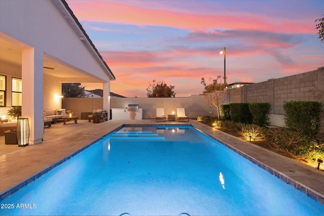 pool at dusk with outdoor lounge area, exterior kitchen, and a patio area