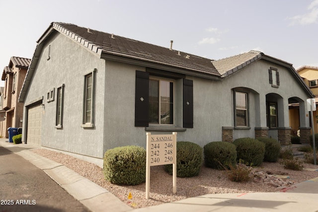 view of front of house featuring stucco siding, a tiled roof, and a garage