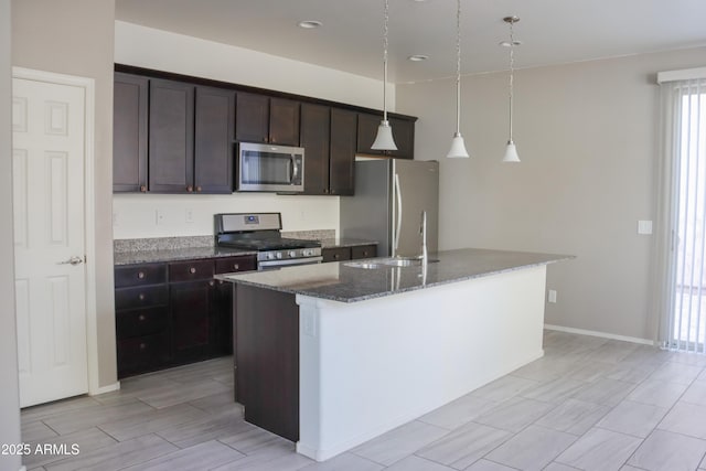 kitchen with an island with sink, dark stone countertops, a sink, appliances with stainless steel finishes, and dark brown cabinets