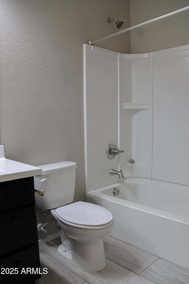 full bath featuring toilet, vanity, a textured wall, and washtub / shower combination