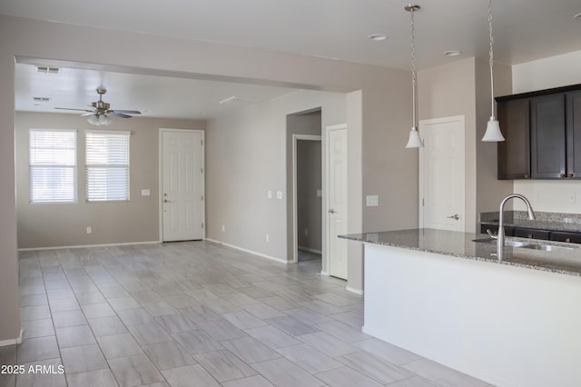 kitchen featuring baseboards, stone counters, ceiling fan, a sink, and dark brown cabinetry