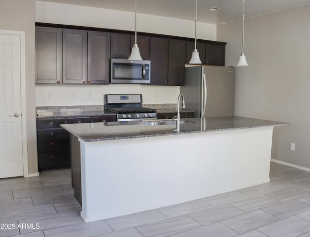 kitchen with a kitchen island with sink, dark brown cabinetry, appliances with stainless steel finishes, stone counters, and hanging light fixtures