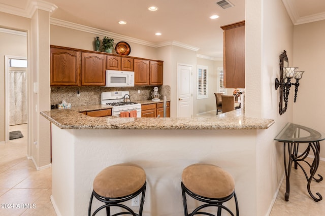 kitchen featuring backsplash, light stone counters, a kitchen breakfast bar, and white appliances