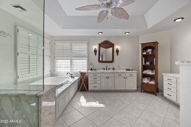 bathroom featuring a tub, tile patterned flooring, vanity, ceiling fan, and a tray ceiling