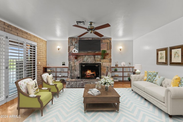 living room featuring brick wall, ceiling fan, a stone fireplace, and light wood-type flooring