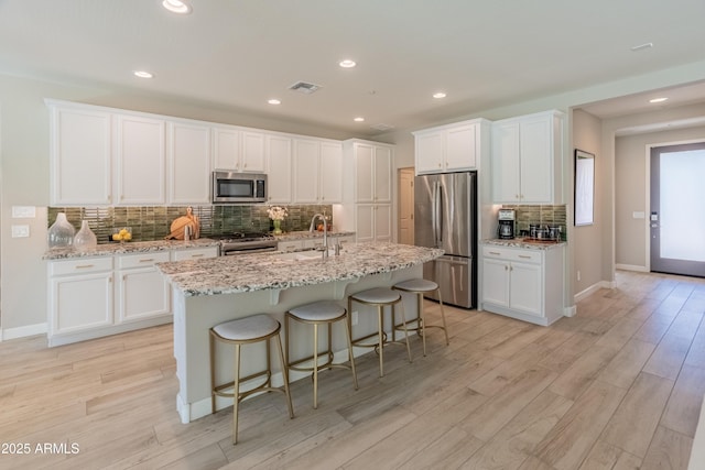 13186 W Via Dona Rd, Peoria, AZ 85383 - kitchen featuring appliances with stainless steel finishes, backsplash, light wood-type flooring, white cabinetry, and an island with sink