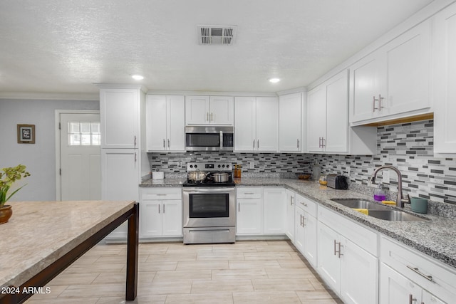 kitchen featuring light stone countertops, decorative backsplash, stainless steel appliances, white cabinets, and sink