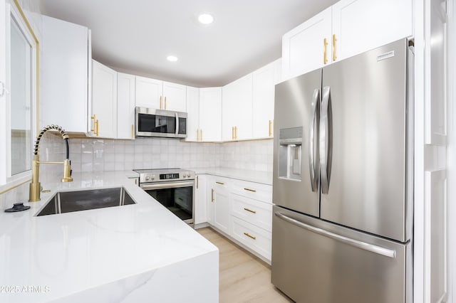 8341 E Keim Dr, Scottsdale, AZ 85250 - kitchen featuring appliances with stainless steel finishes, light stone counters, tasteful backsplash, white cabinetry, and light wood-style flooring