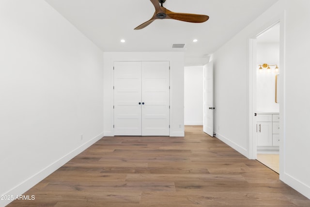 unfurnished bedroom featuring wood-type flooring, a closet, ceiling fan, and ensuite bathroom