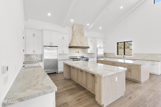 kitchen with premium range hood, a spacious island, beamed ceiling, range, and stainless steel refrigerator