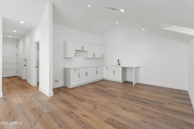 kitchen with light wood-type flooring, white cabinetry, sink, and high vaulted ceiling