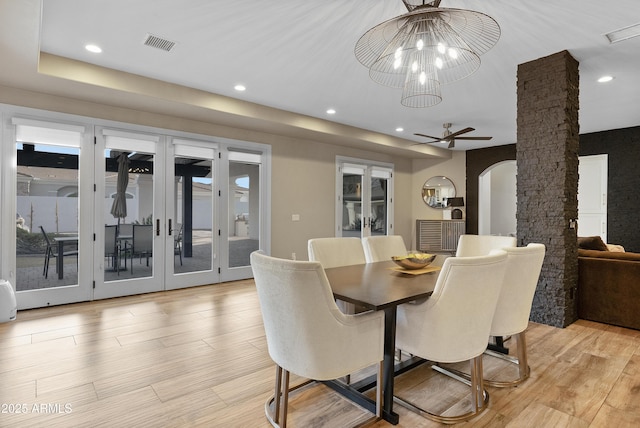 dining space with ceiling fan with notable chandelier, light hardwood / wood-style floors, french doors, and decorative columns