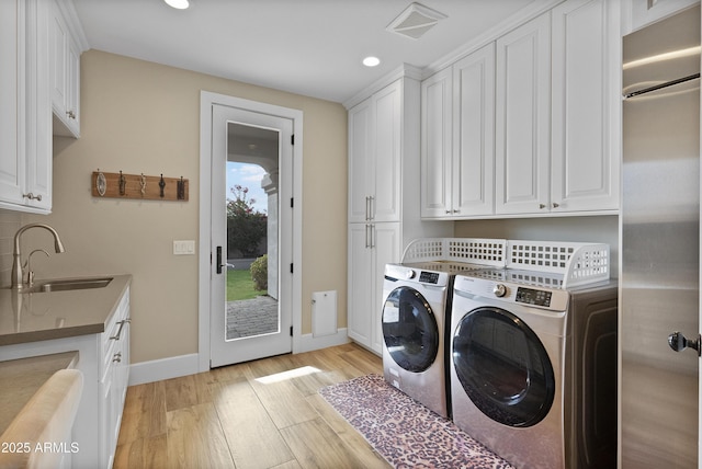 laundry area featuring washer and dryer, cabinets, light wood-type flooring, and sink