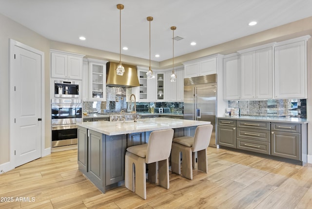 kitchen with light stone countertops, stainless steel appliances, decorative light fixtures, white cabinets, and an island with sink