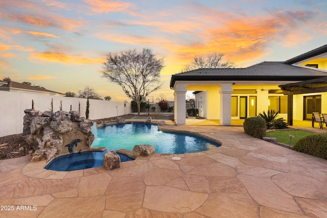 pool at dusk featuring pool water feature, a patio area, and an in ground hot tub