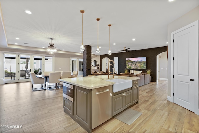 kitchen featuring hanging light fixtures, light stone counters, a kitchen island with sink, and sink