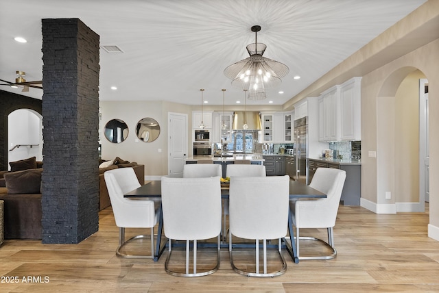 dining room with ornate columns, light hardwood / wood-style floors, and ceiling fan with notable chandelier