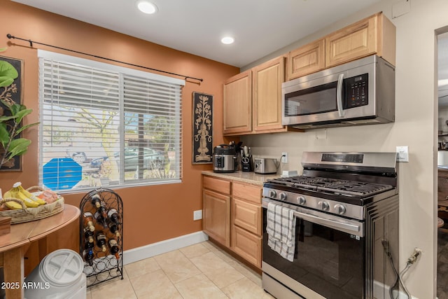 kitchen featuring light tile patterned floors, stainless steel appliances, light countertops, light brown cabinets, and baseboards