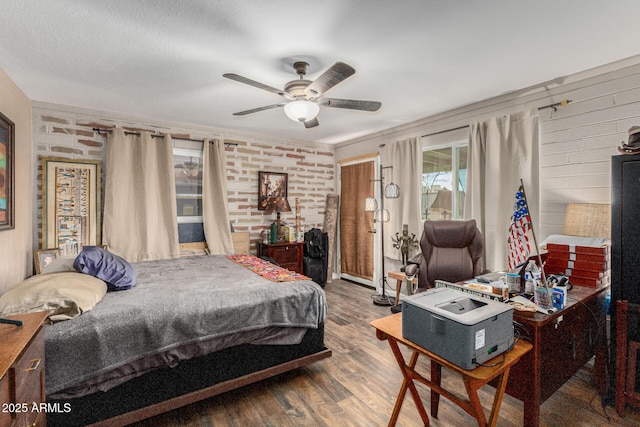 bedroom with ceiling fan, brick wall, and wood finished floors