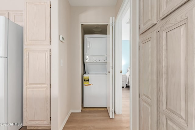 washroom with light wood-type flooring, laundry area, baseboards, and stacked washer / dryer