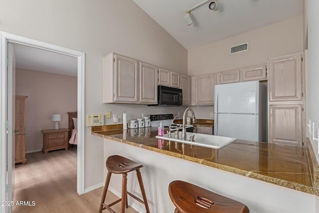 kitchen featuring white appliances, visible vents, a kitchen breakfast bar, light wood-type flooring, and a sink