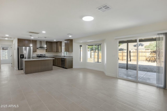 kitchen featuring hanging light fixtures, wall chimney exhaust hood, sink, a kitchen island, and stainless steel appliances