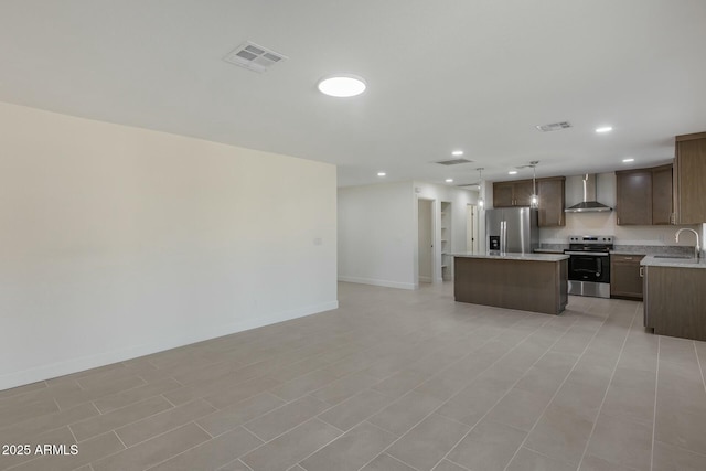 kitchen featuring a kitchen island, wall chimney range hood, stainless steel appliances, sink, and hanging light fixtures