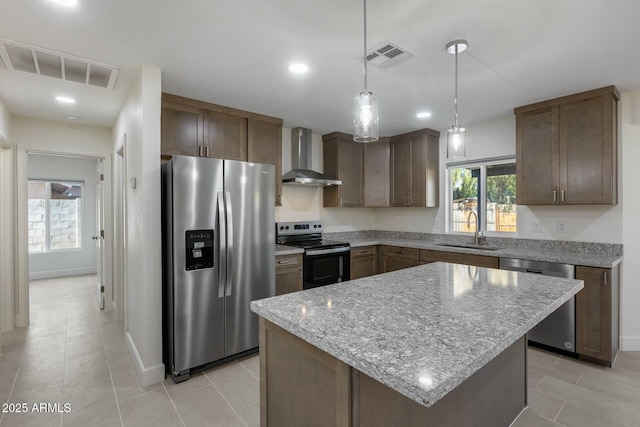 kitchen with a center island, wall chimney exhaust hood, stainless steel appliances, sink, and hanging light fixtures