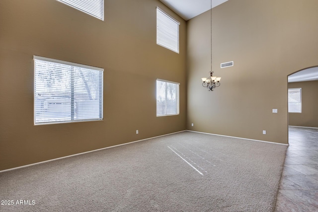 spare room featuring carpet floors, a high ceiling, and a chandelier