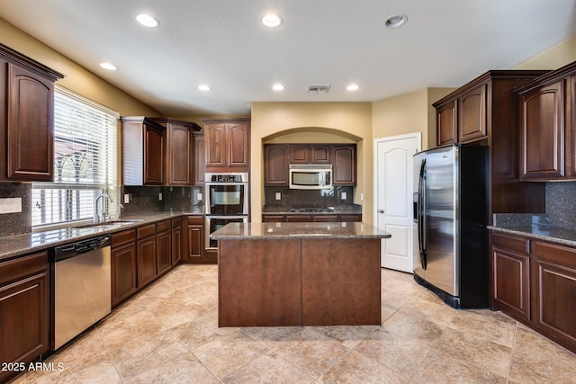 kitchen featuring dark stone counters, appliances with stainless steel finishes, sink, and a center island