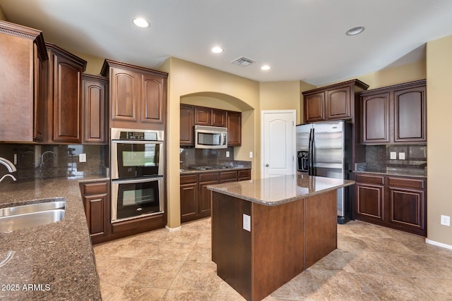 kitchen with a kitchen island, stainless steel appliances, dark stone counters, tasteful backsplash, and sink