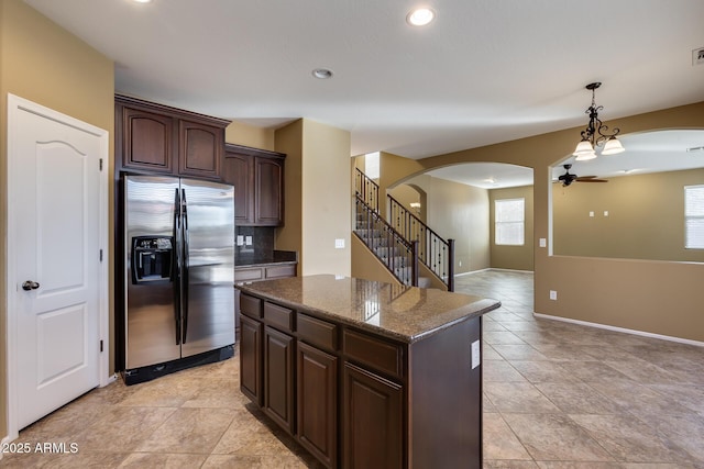 kitchen featuring stainless steel refrigerator with ice dispenser, dark stone countertops, decorative backsplash, ceiling fan, and dark brown cabinets