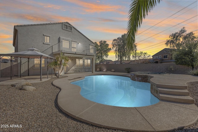 pool at dusk featuring an in ground hot tub, a gazebo, and a patio