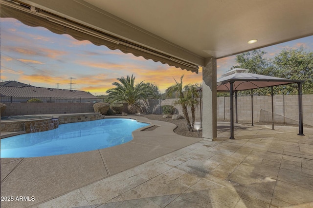 pool at dusk with an in ground hot tub, a patio area, and a gazebo