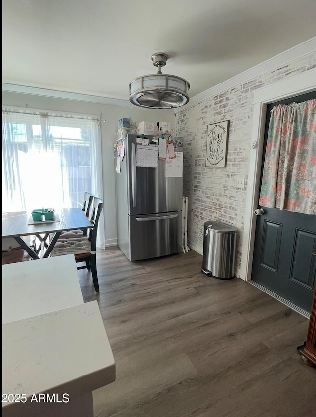 kitchen with crown molding, dark hardwood / wood-style floors, stainless steel fridge, and brick wall