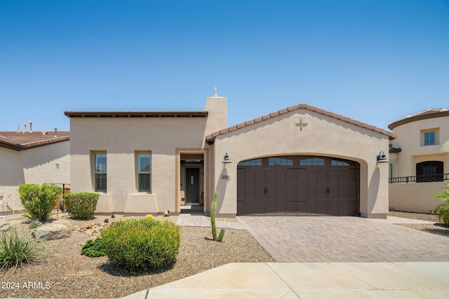 mediterranean / spanish-style home featuring a garage, decorative driveway, a tile roof, and stucco siding