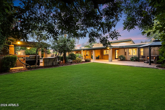 back house at dusk with a yard and a patio area