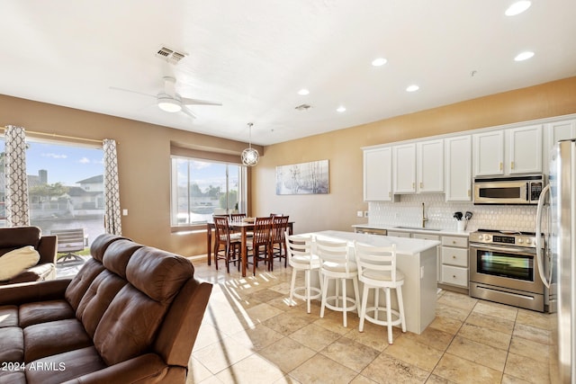 kitchen featuring a kitchen island, appliances with stainless steel finishes, pendant lighting, white cabinetry, and sink