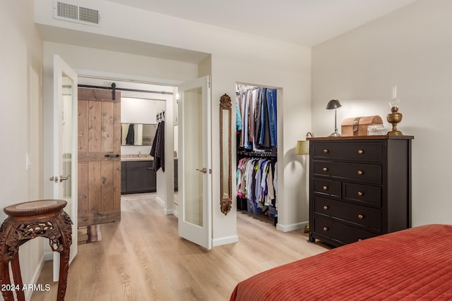 bedroom featuring sink, a barn door, connected bathroom, light hardwood / wood-style floors, and a closet