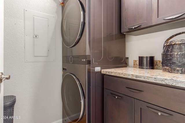 laundry room featuring stacked washer / dryer, electric panel, and cabinets